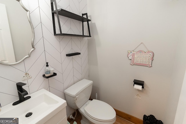 half bath featuring a sink, toilet, baseboards, and tile walls