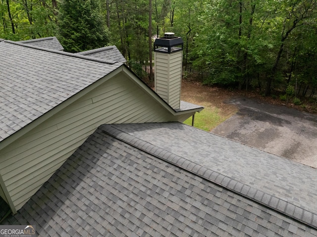 exterior view of a shingled roof, a chimney, and a wooded view