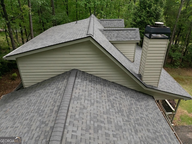 view of side of home featuring a chimney, a shingled roof, and a forest view