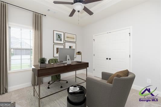 office space with ceiling fan, a tray ceiling, baseboards, and light colored carpet