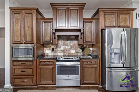 kitchen featuring stainless steel appliances, ornamental molding, tasteful backsplash, dark stone counters, and baseboards