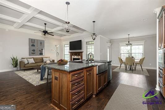 kitchen featuring a sink, baseboards, a fireplace, dark wood-type flooring, and beamed ceiling