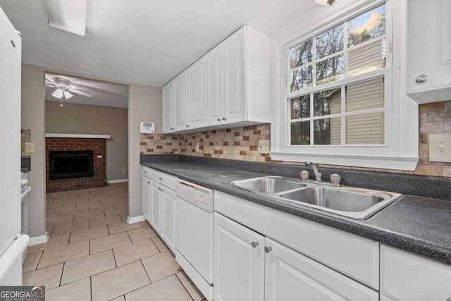 kitchen with white dishwasher, a sink, dark countertops, and white cabinets