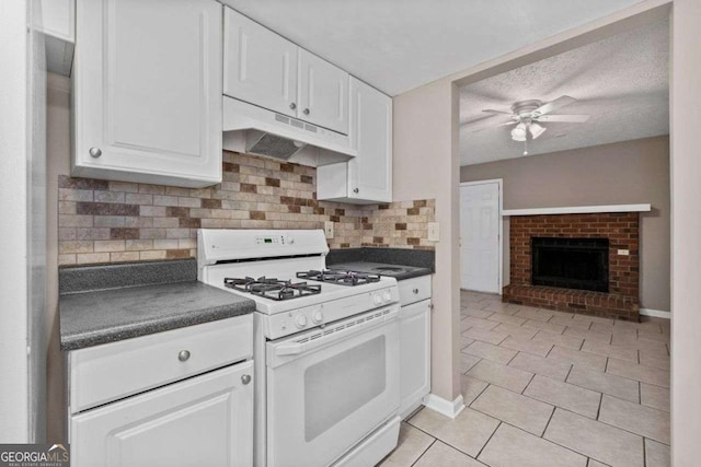 kitchen with white range with gas stovetop, under cabinet range hood, dark countertops, ceiling fan, and white cabinetry
