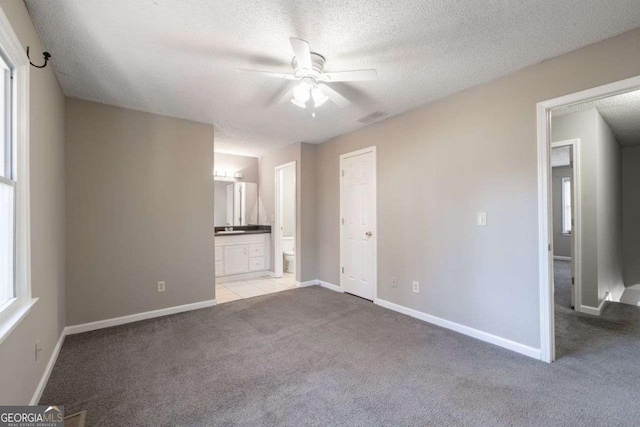 unfurnished bedroom featuring light colored carpet, a textured ceiling, ensuite bath, baseboards, and ceiling fan