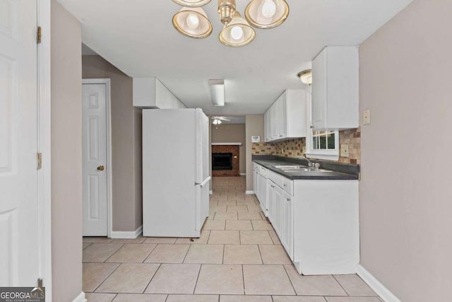 kitchen with freestanding refrigerator, dark countertops, a sink, and white cabinets