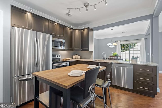 kitchen with appliances with stainless steel finishes, a peninsula, dark brown cabinetry, crown molding, and butcher block countertops