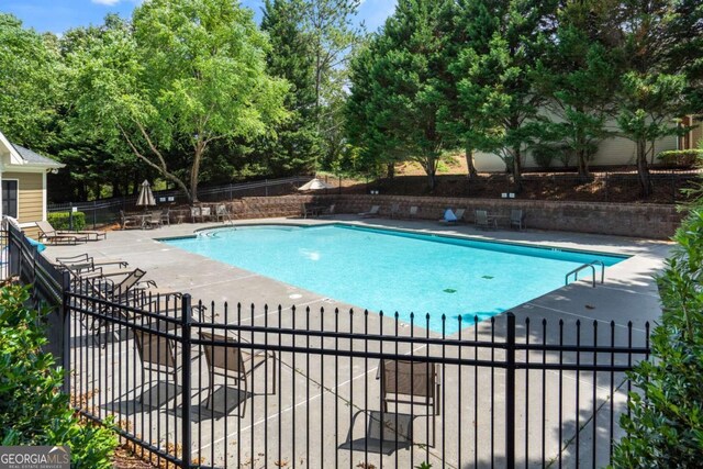 community pool with fence, a patio, and view of scattered trees