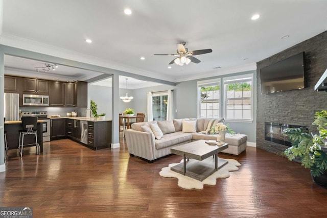 living room featuring a fireplace, ceiling fan, ornamental molding, dark wood-type flooring, and baseboards