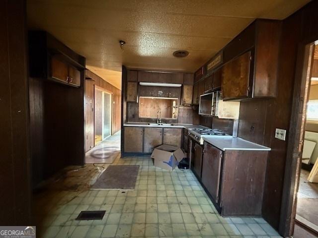 kitchen featuring light floors, open shelves, a sink, wooden walls, and dark brown cabinets
