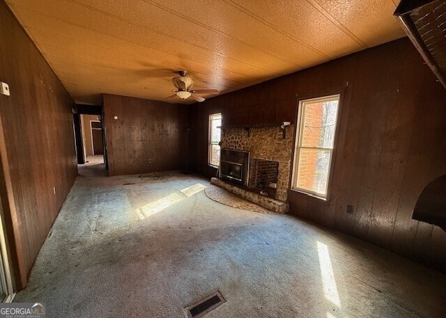 unfurnished living room featuring wood walls, ceiling fan, a fireplace, and carpet flooring