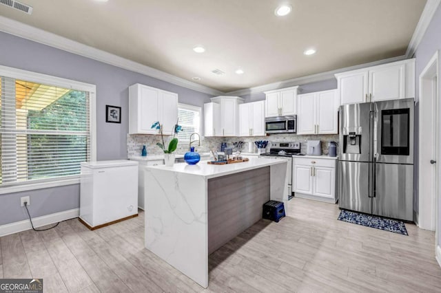 2102 Braswell Ln, Loganville, GA 30052 - kitchen with stainless steel appliances, ornamental molding, tasteful backsplash, white cabinetry, and light wood-style floors