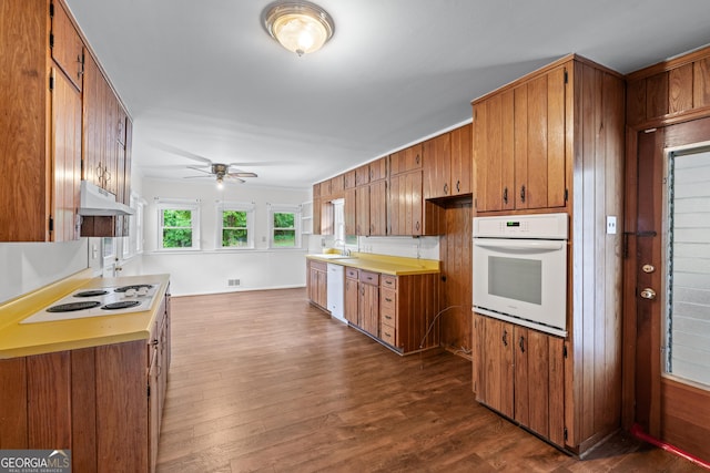 kitchen with white appliances, brown cabinets, under cabinet range hood, ceiling fan, and dark wood-style floors