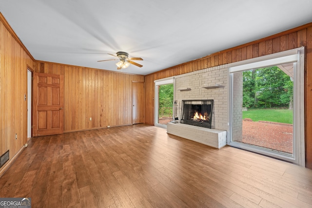 unfurnished living room featuring ceiling fan, plenty of natural light, a fireplace, wood-type flooring, and wood walls