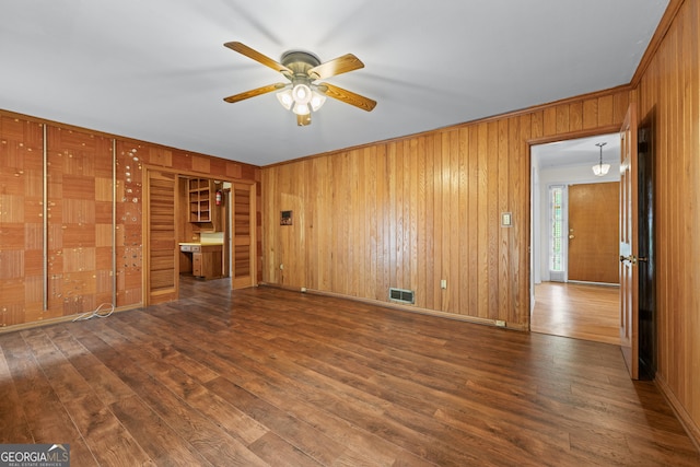empty room with ceiling fan, wood finished floors, wooden walls, baseboards, and crown molding