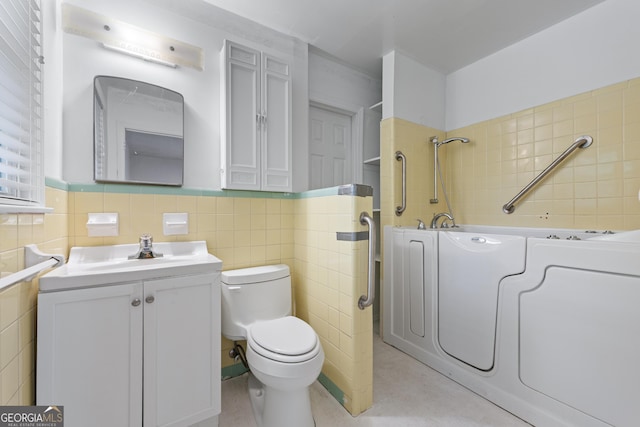 bathroom with tile walls, a tub, toilet, vanity, and a wainscoted wall