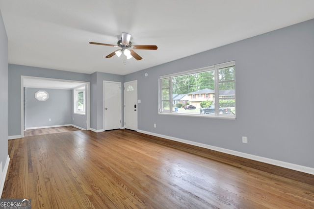 unfurnished living room with plenty of natural light, a ceiling fan, baseboards, and wood finished floors