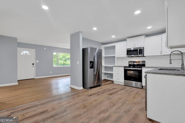 kitchen featuring appliances with stainless steel finishes, a sink, white cabinets, light wood finished floors, and recessed lighting