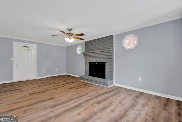 unfurnished living room with a ceiling fan, wood finished floors, baseboards, a fireplace, and ornamental molding