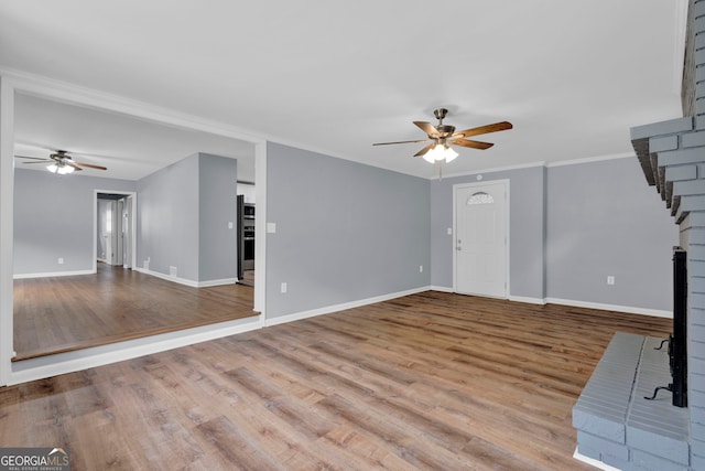 unfurnished living room featuring ceiling fan, baseboards, wood finished floors, and ornamental molding