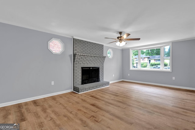 unfurnished living room with ornamental molding, ceiling fan, a fireplace, baseboards, and light wood-style flooring
