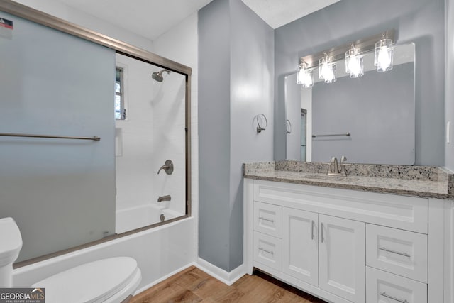 bathroom featuring toilet, wood finished floors, combined bath / shower with glass door, and baseboards
