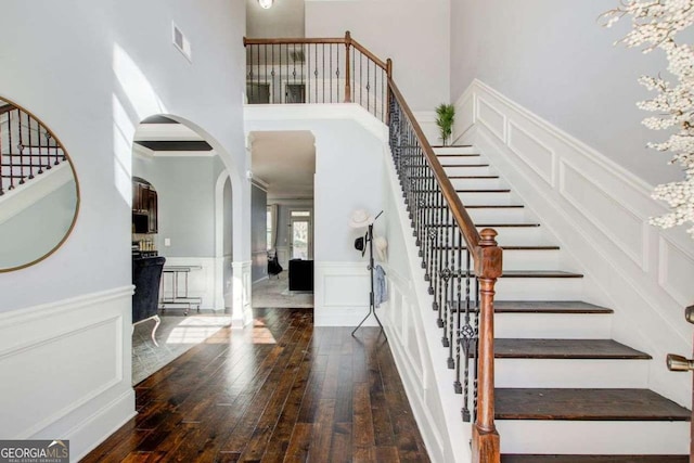 7933 Heathmore Dr, Fairburn, GA 30213 - stairway featuring a towering ceiling, hardwood / wood-style floors, a decorative wall, arched walkways, and crown molding