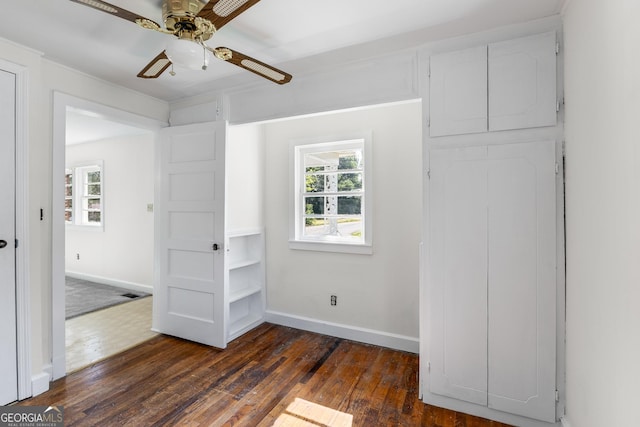 unfurnished bedroom with multiple windows, dark wood-type flooring, baseboards, and ceiling fan