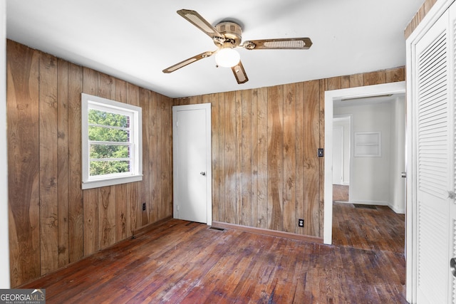 unfurnished bedroom with wooden walls, hardwood / wood-style flooring, ceiling fan, and a closet