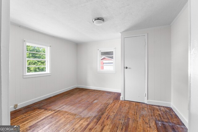 unfurnished room featuring wood-type flooring, baseboards, and a textured ceiling
