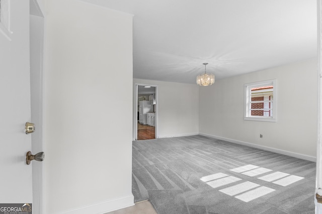 carpeted empty room with a chandelier and baseboards