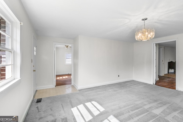 carpeted empty room with a chandelier, baseboards, and ceiling fan