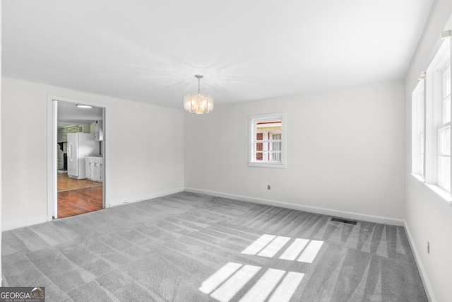 carpeted spare room featuring a chandelier, healthy amount of natural light, and baseboards