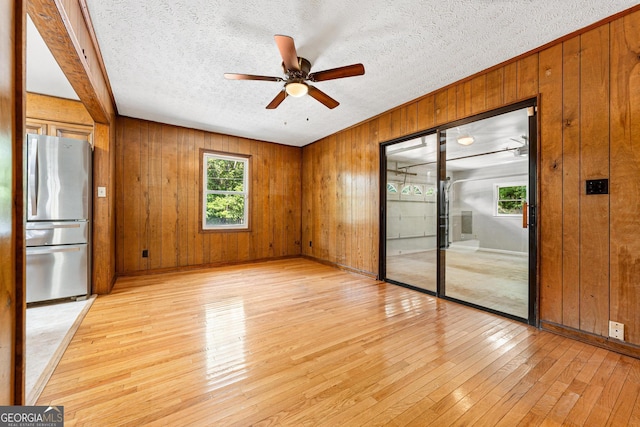 empty room with light wood-style floors, wood walls, ceiling fan, a textured ceiling, and baseboards