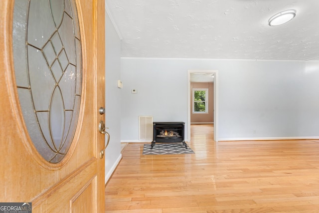 foyer featuring light wood finished floors, crown molding, a textured ceiling, and baseboards
