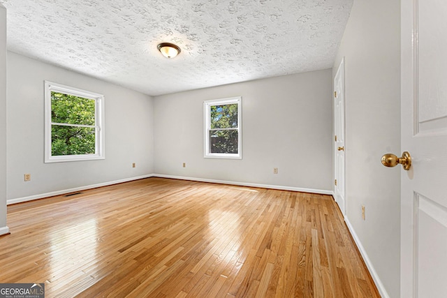 spare room featuring a textured ceiling, light wood-type flooring, and baseboards