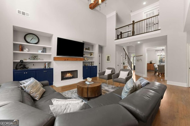 living area featuring stairs, built in shelves, a warm lit fireplace, wood finished floors, and a high ceiling