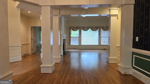 hallway with decorative columns, wood finished floors, crown molding, a decorative wall, and wainscoting