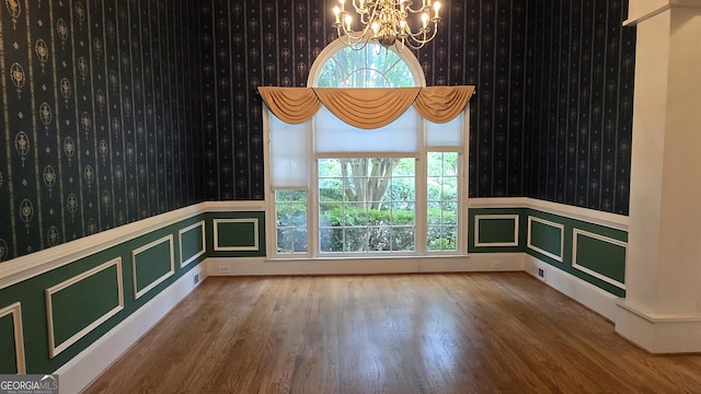 unfurnished dining area with wallpapered walls, a chandelier, wainscoting, wood finished floors, and healthy amount of natural light