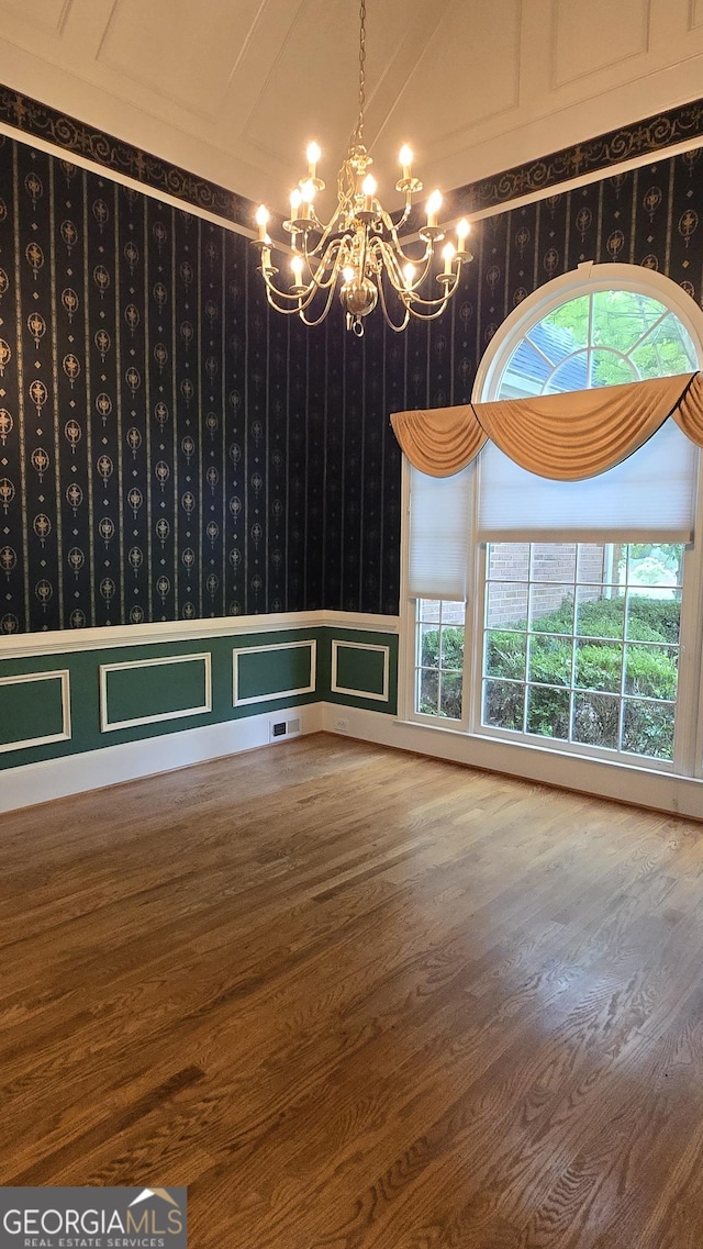 empty room with a chandelier, wallpapered walls, wood finished floors, and a wainscoted wall