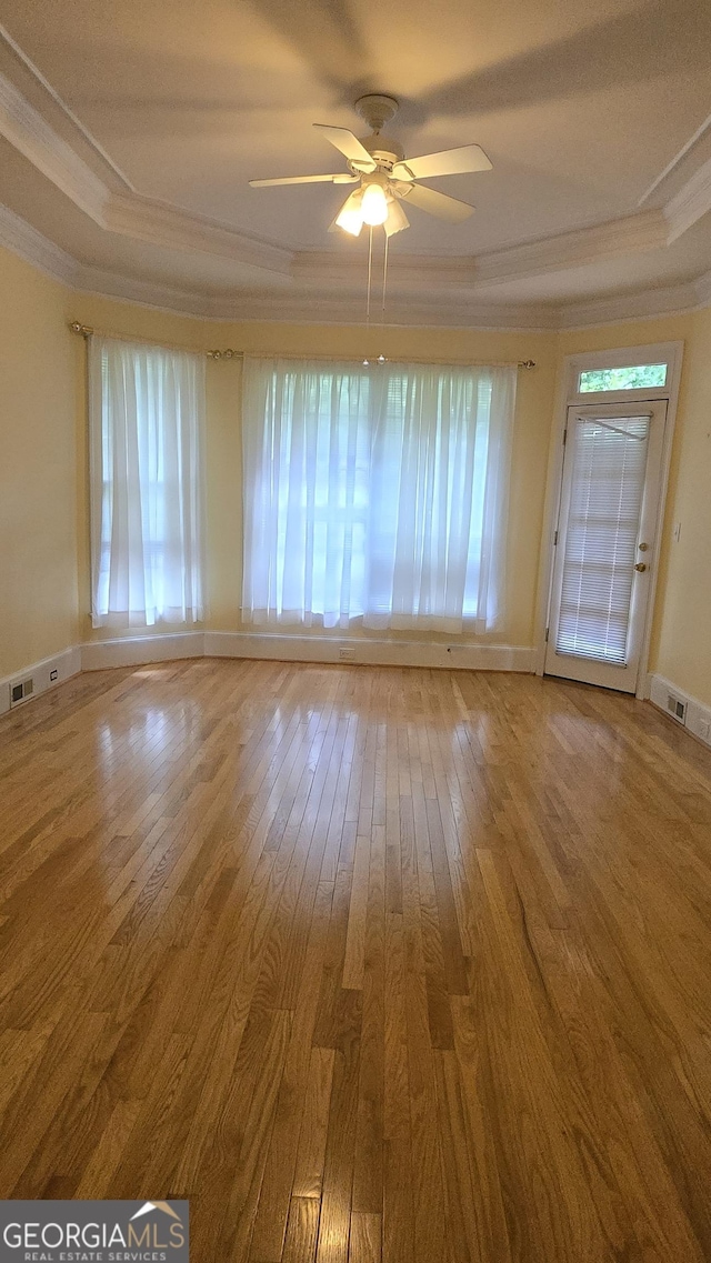 empty room featuring crown molding, a raised ceiling, wood-type flooring, ceiling fan, and baseboards
