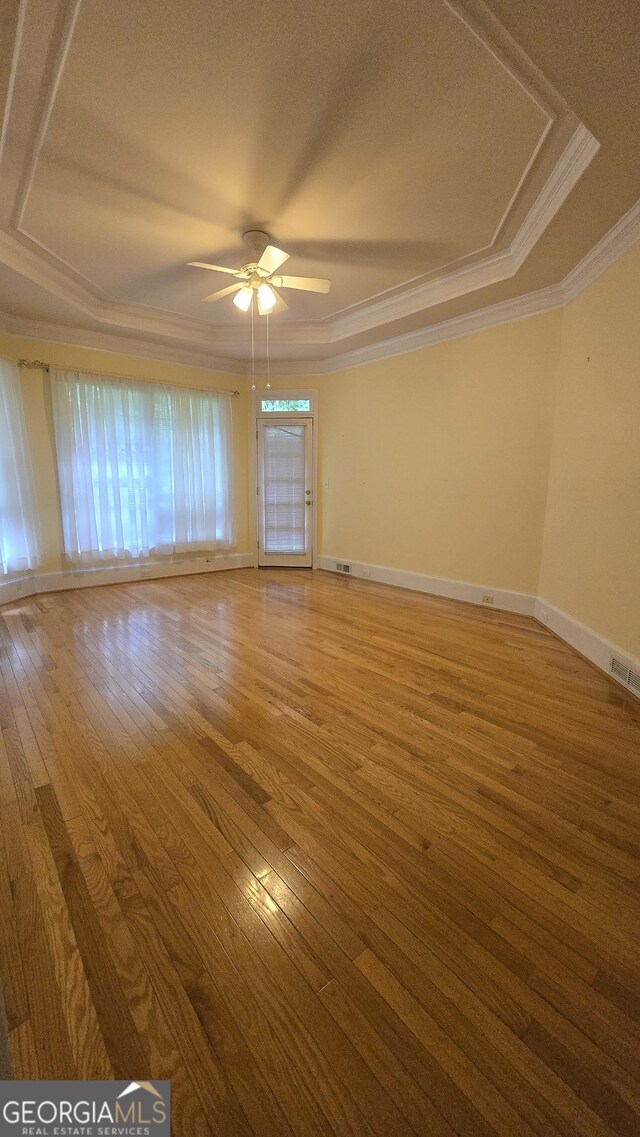 unfurnished room featuring a ceiling fan, wood-type flooring, crown molding, a raised ceiling, and baseboards