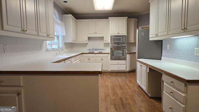 kitchen featuring stainless steel appliances, a sink, a peninsula, dark wood-type flooring, and tasteful backsplash