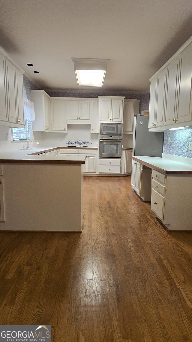 kitchen featuring stainless steel appliances, dark wood-style floors, white cabinetry, light countertops, and a peninsula