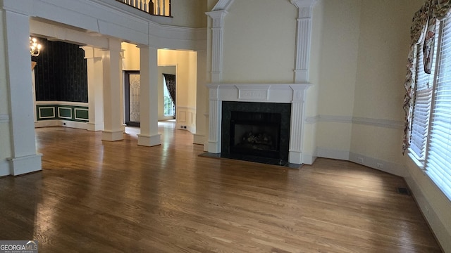 unfurnished living room featuring ornate columns, wood finished floors, and a high end fireplace