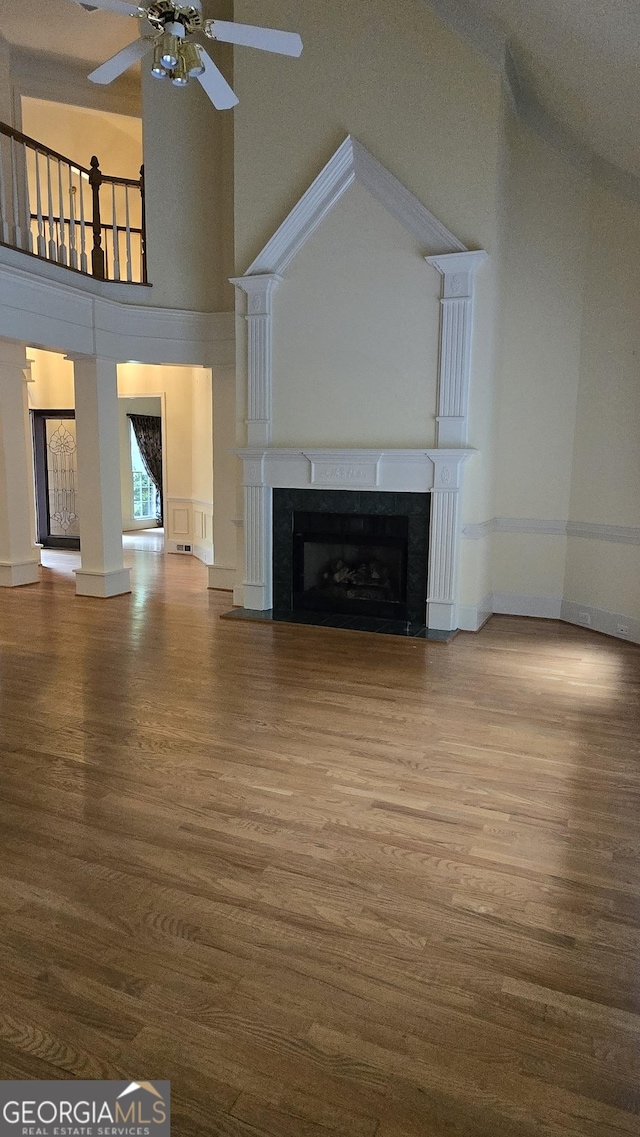 unfurnished living room featuring ceiling fan, wood finished floors, a fireplace, a towering ceiling, and baseboards