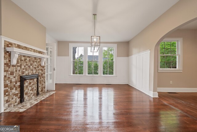 409 N Jefferson Ave, Eatonton, GA 31024 - unfurnished living room with wood-type flooring, wainscoting, a decorative wall, arched walkways, and a tile fireplace