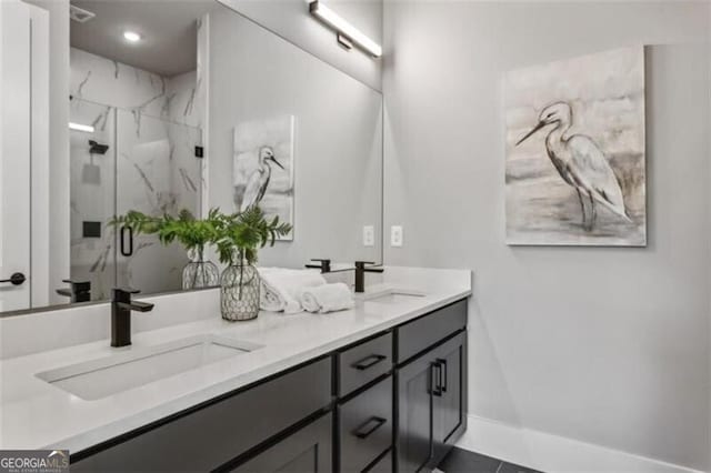 bathroom with a marble finish shower, double vanity, and baseboards