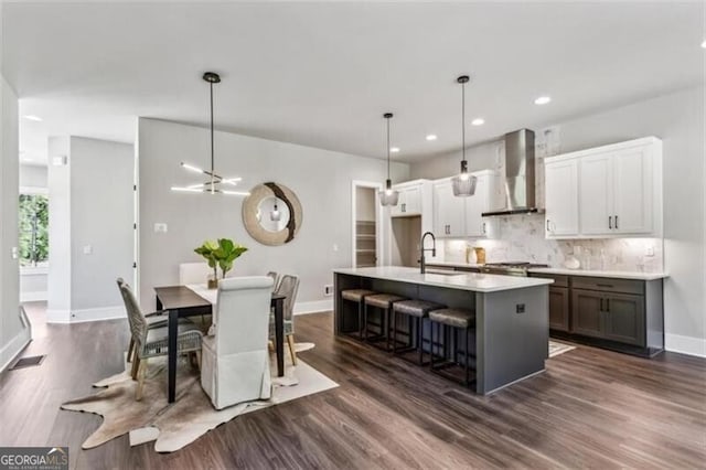 kitchen featuring wall chimney range hood, a sink, baseboards, dark wood-style floors, and backsplash
