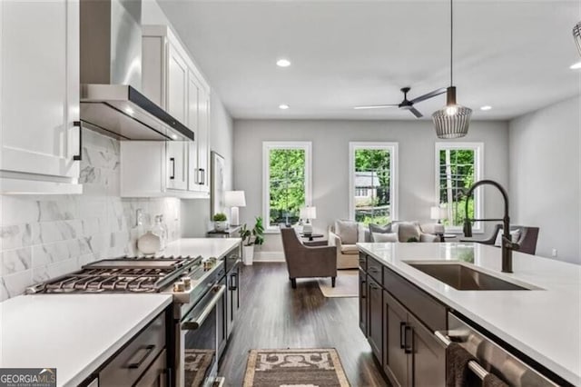 kitchen featuring wall chimney range hood, appliances with stainless steel finishes, a sink, light countertops, and recessed lighting